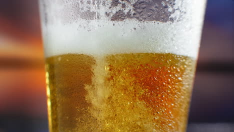 Cerveza-Fría-Macro-En-Cámara-Lenta-Se-Vierte-En-Un-Vaso-Con-Transpiración.-Las-Burbujas-De-Cerveza-Suben-A-La-Superficie.